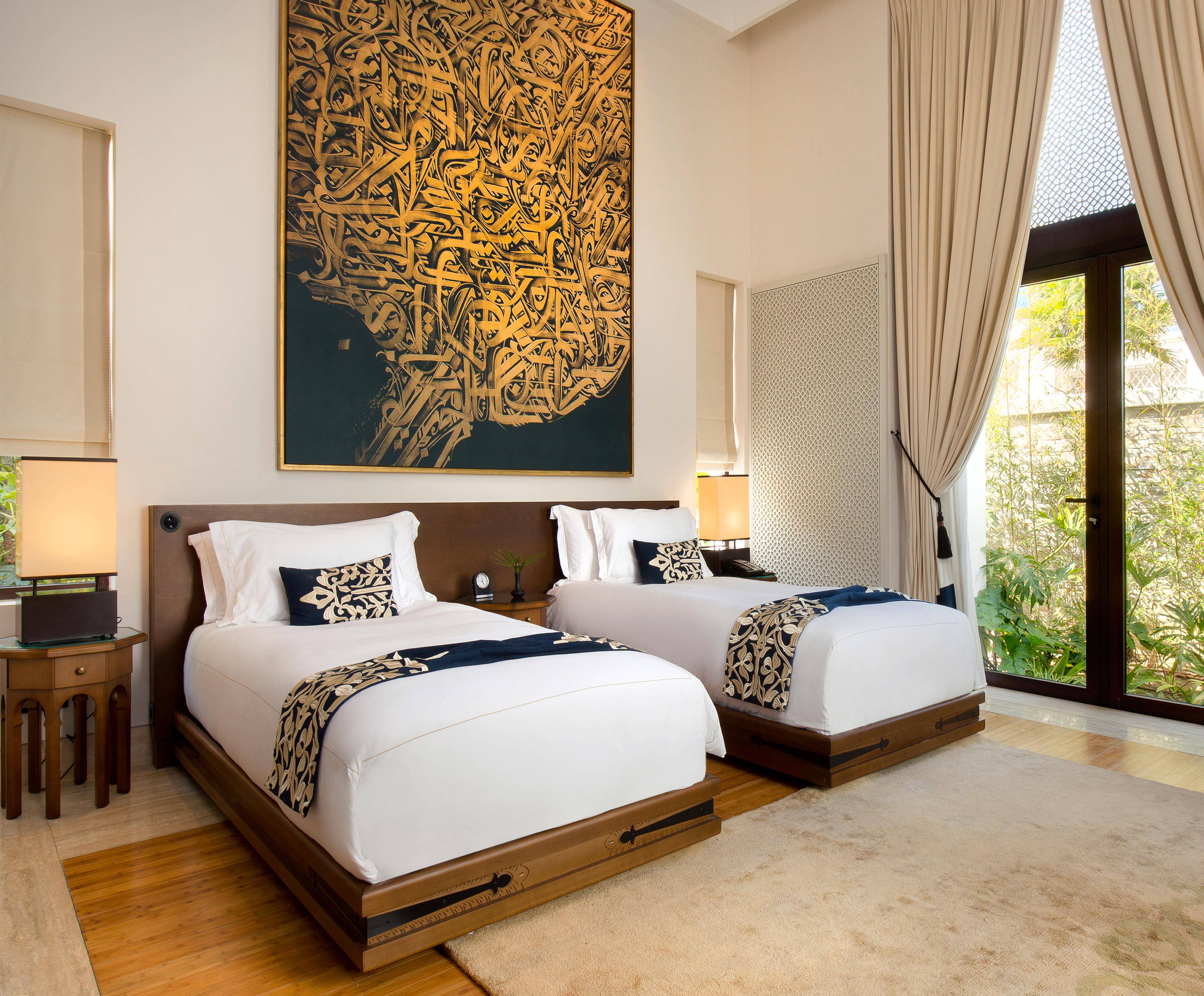 Two twin beds with elegant bedding in Banyan Tree Tamouda Bay room, large art piece above.